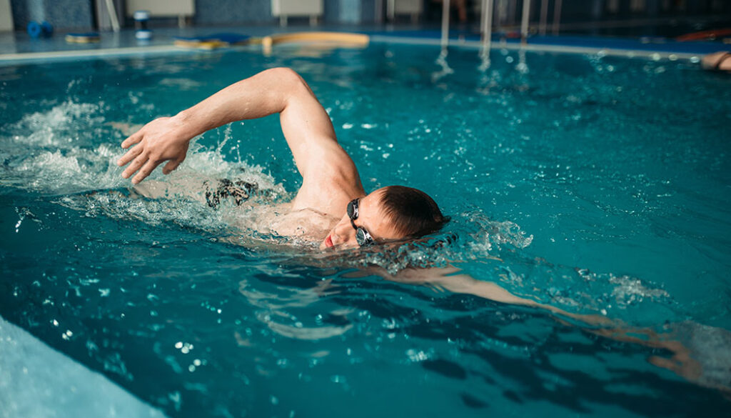 Male swimmer swims on workout in swimming pool