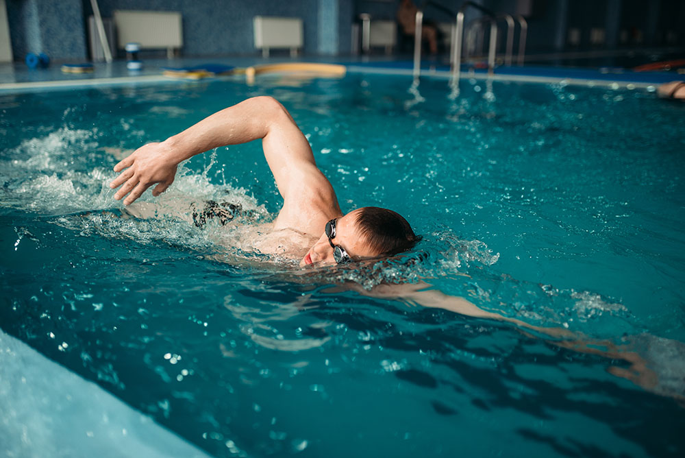 Male swimmer swims on workout in swimming pool